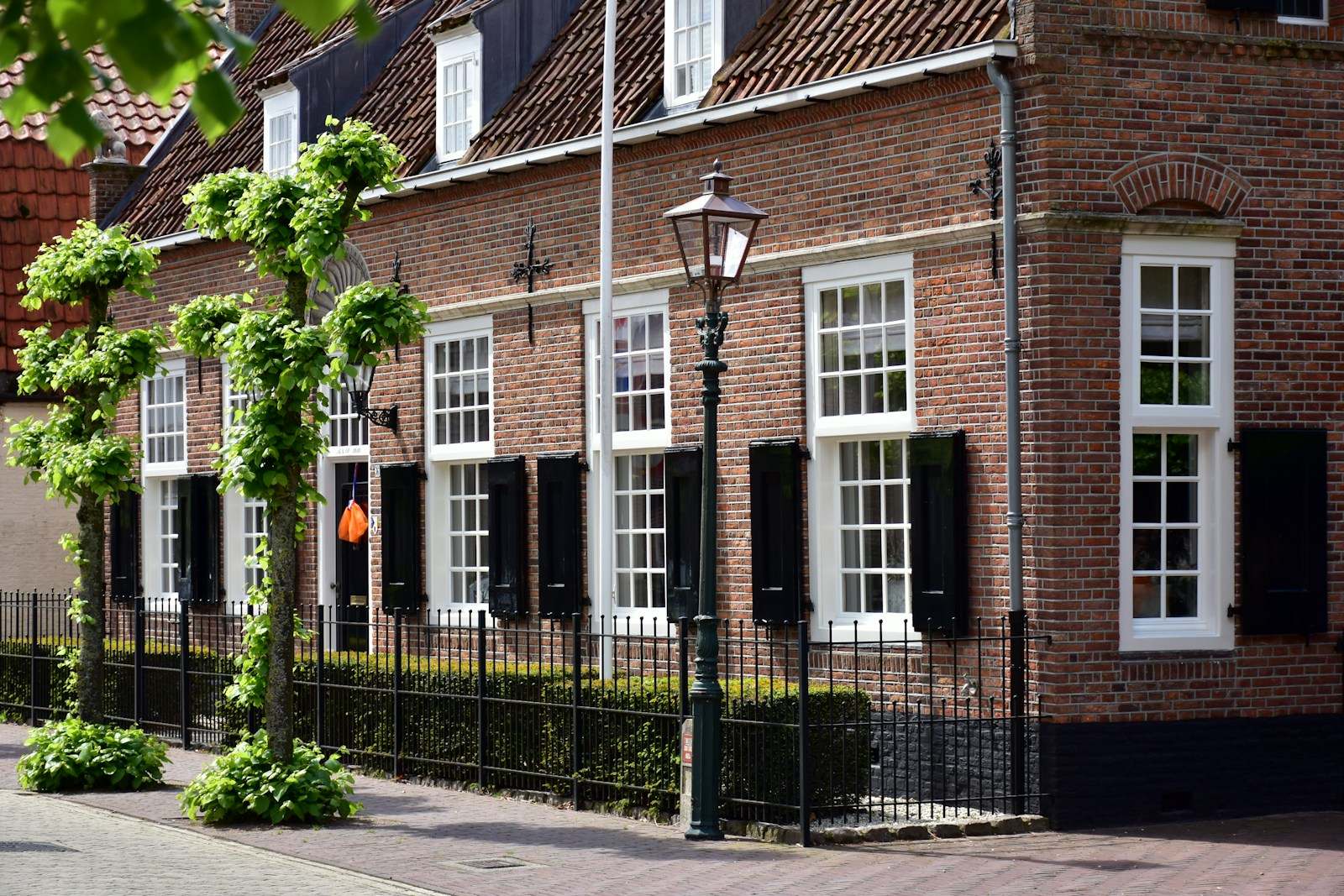 Bakstenen woningen met witte ramen en zwarte luiken achter een smeedijzeren hek