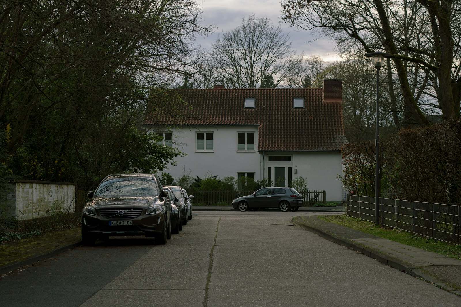 Witte woning met een donker pannendak aan het einde van een straat met geparkeerde auto's